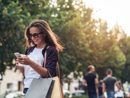 a woman holding shopping bags and looking at her cell phone.